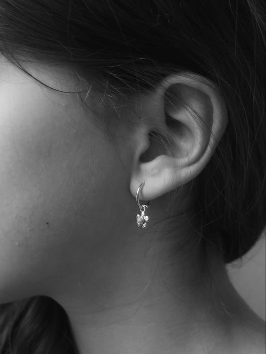 Záběr na ucho dívky ze strany s Rubari náušničkami Moonhoops z pravého 14kt zlata a kytičkou s tyrkysem na černobílé fotografii.